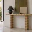A modern wooden console table with blocky striped legs, styled with a black table lamp and books in a minimalist interior setting.