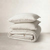 Two off-white linen pillowcases stacked on a folded quilt cover, frayed edges showing