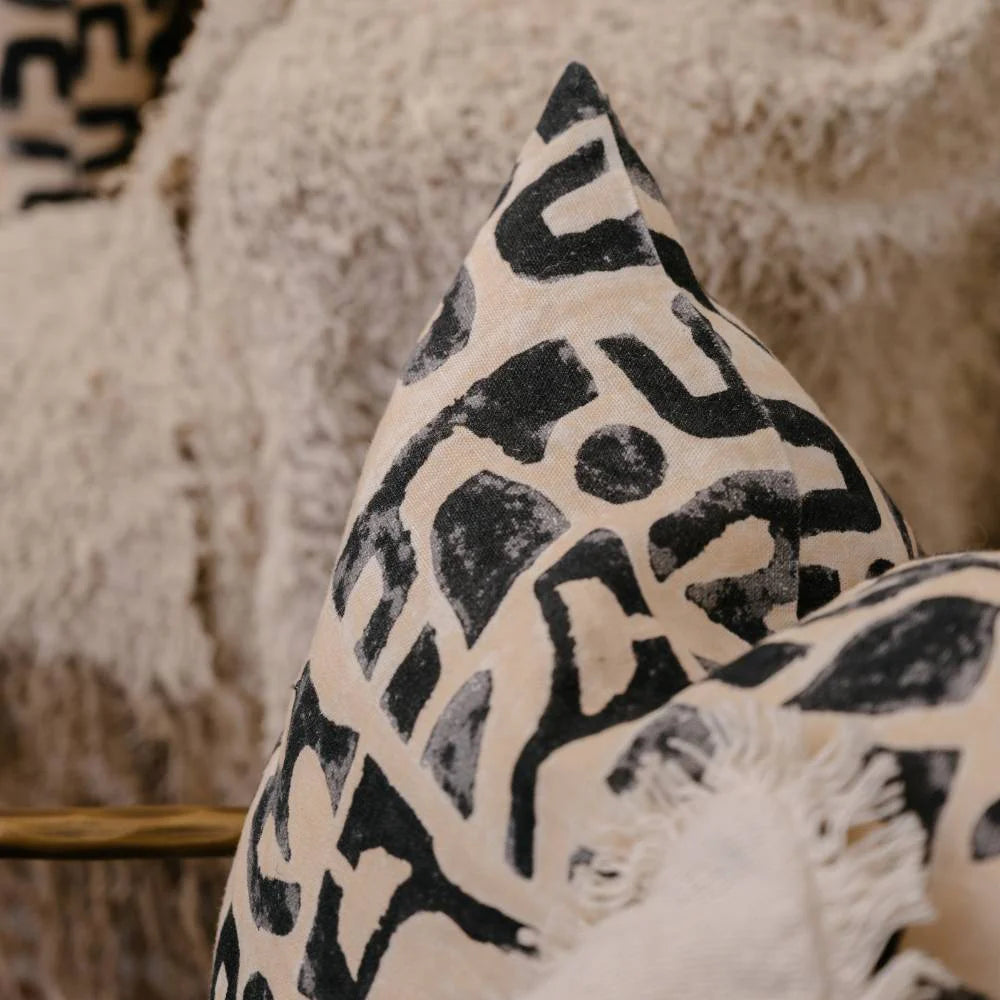 Abstract black print cushion on nude linen, styled on chair with boucle throw