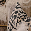 Abstract black print cushion on nude linen, styled on chair with boucle throw