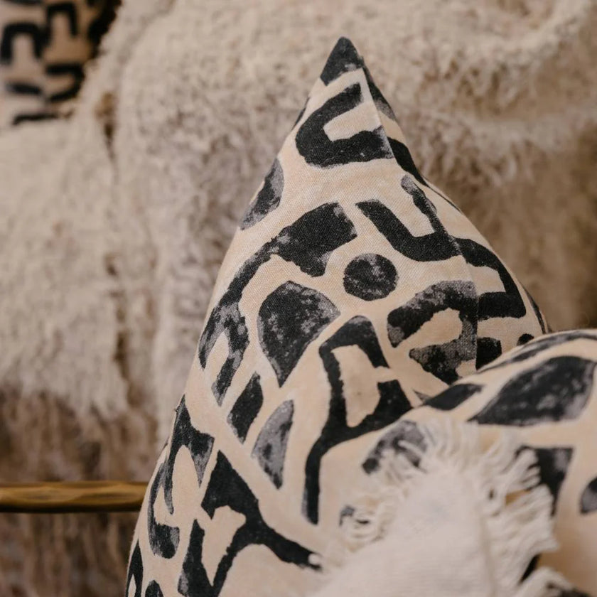 Abstract black print cushion on nude linen, styled on chair with boucle throw