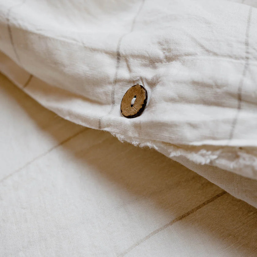 Coconut button fastening the folded edge of an off-white French linen quilt cover