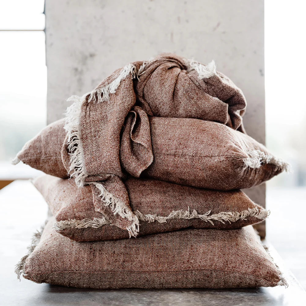 Tabako Linen Cushion — stack of textured tobacco linen cushions with frayed edges
