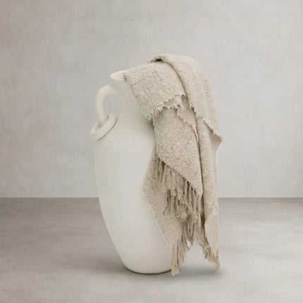 Chunky knit throw in natural draped over white ceramic vase, styled product shot
