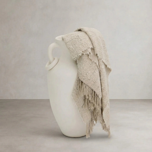 Chunky knit throw in natural draped over white ceramic vase, styled product shot