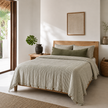 Bed made up with an olive pencil stripe French linen quilt cover in a light bedroom