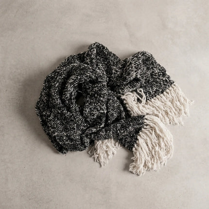 Chunky knit throw in charcoal with cream tassel fringe, flat lay on neutral background