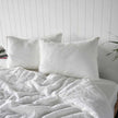 Two white linen pillows with frayed edges against a panelled wall, quilt cover thrown back