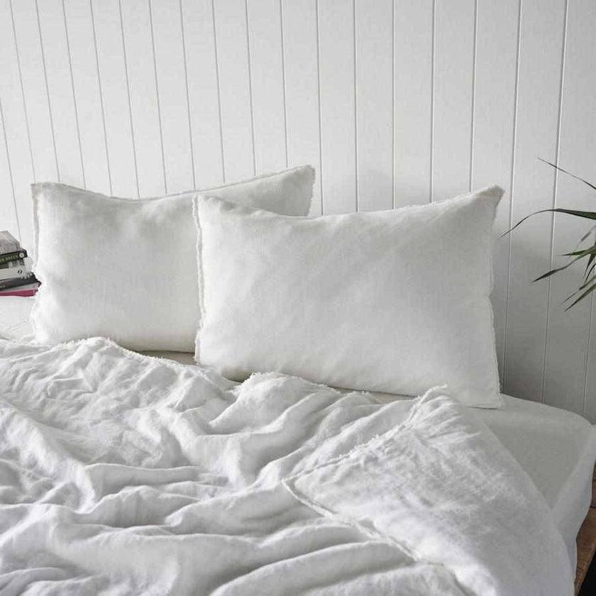 Two white linen pillows with frayed edges against a panelled wall, quilt cover thrown back