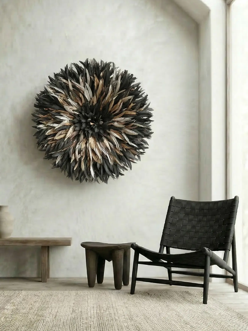 Senufo feather juju hat wall hanging in dark tones, styled with black leather chair and timber stool
