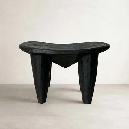 Senufo black stool, side angle view on neutral background showing organic carved form